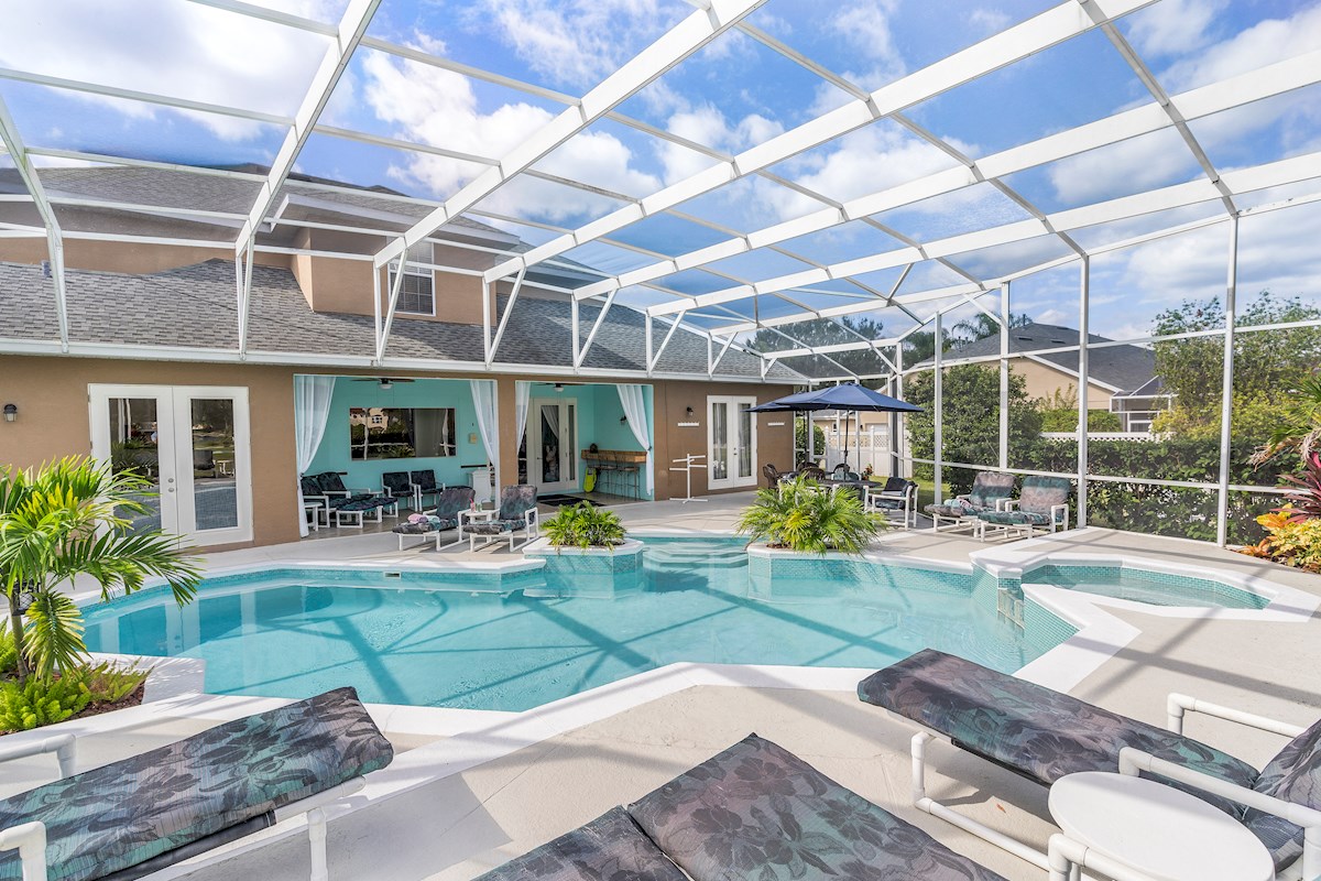 Gorgeous large tropical pool area with spa, surrounded by palm trees and shrubs.