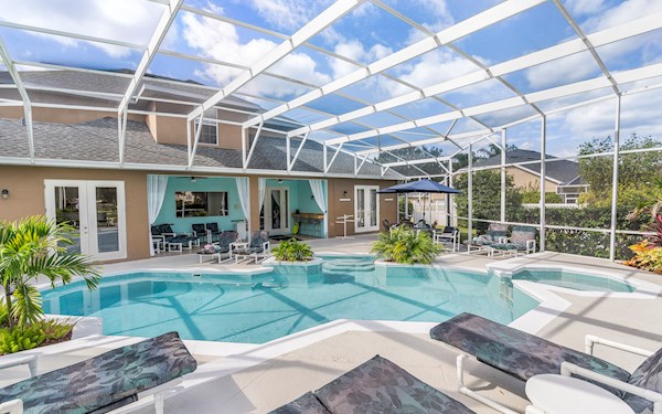 Gorgeous large tropical pool area with spa, surrounded by palm trees and shrubs.